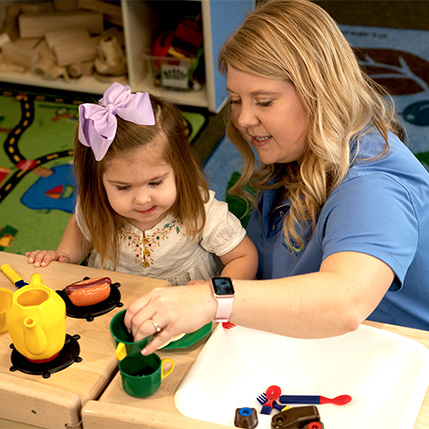 teacher and child playing with pretend kitchen accessories
